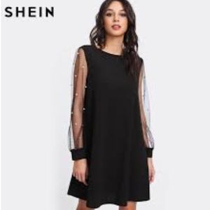 A black dress with mesh sleeves and a pearl detail